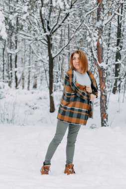 Ekose bir elbiseye sarılmış ve kış ormanında yürüyüş yapan mutlu bir genç kız. Noel tatilinde yürüyüş, seçici bir odak..