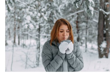 Gri ceketli ve beyaz eldivenli güzel bir kız karlı bir ormanda içki içiyor. Kış mevsiminde konfor ve sıcaklık. seçici odak.