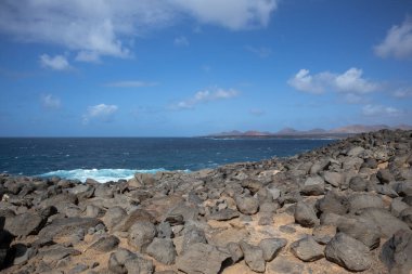 Atlantik Okyanusu 'nun kayalık kıyısı. Lav taşları kahverengiden siyaha boyanmış. Sakin su. Baharda açık bulutlu mavi gökyüzü. Playa Blanca, Lanzarote, Kanarya Adaları, İspanya.