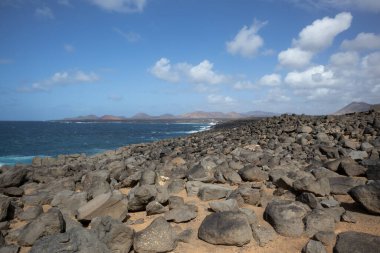 Atlantik Okyanusu 'nun kayalık kıyısı. Lav taşları kahverengiden siyaha boyanmış. Sakin su. Baharda açık bulutlu mavi gökyüzü. Playa Blanca, Lanzarote, Kanarya Adaları, İspanya.