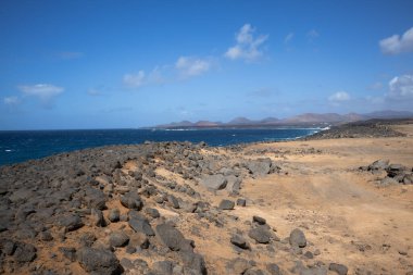 Atlantik Okyanusu 'nun kayalık kıyısı. Lav taşları kahverengiden siyaha boyanmış. Sakin su. Baharda açık bulutlu mavi gökyüzü. Playa Blanca, Lanzarote, Kanarya Adaları, İspanya.