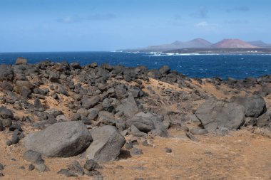 Atlantik Okyanusu 'nun kayalık kıyısı. Lav taşları kahverengiden siyaha boyanmış. Sakin su. Baharda açık bulutlu mavi gökyüzü. Playa Blanca, Lanzarote, Kanarya Adaları, İspanya.