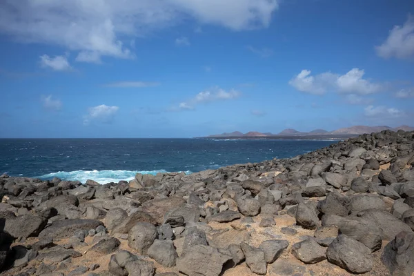 Atlantik Okyanusu 'nun kayalık kıyısı. Lav taşları kahverengiden siyaha boyanmış. Sakin su. Baharda açık bulutlu mavi gökyüzü. Playa Blanca, Lanzarote, Kanarya Adaları, İspanya.