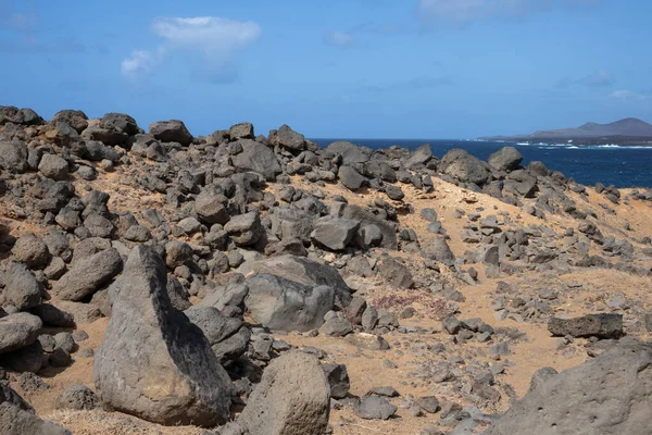 Atlantik Okyanusu 'nun kayalık kıyısı. Lav taşları kahverengiden siyaha boyanmış. Sakin su. Baharda açık bulutlu mavi gökyüzü. Playa Blanca, Lanzarote, Kanarya Adaları, İspanya.
