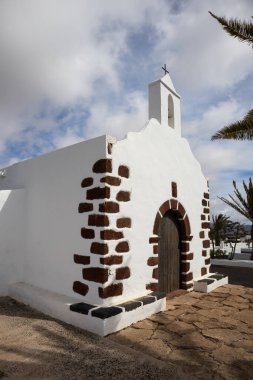 Little church called Ermita de Nuestra Senora de Regla,surrounded by palm trees. Traditional white facade with contrast details .Cloudy late winter day. La Vegueta, Lanzarote, Canarian Islands, Spain.