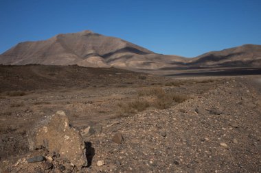 Volkanik kökenli çöl. Bir sürü taş, kaya ve bir tepe var. Mavi yay gökyüzü ve ışık bulutları. Lanzarote, Kanarya Adaları, İspanya.