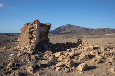 Doğası gereği Playa del Papagayo 'nun yukarısındaki bir tepede bulunan bir borazan yıkıntısı. Parlak mavi gökyüzü. Evin etrafı volkan çölü ile çevrili. Lanzarote, Kanarya Adaları, İspanya.