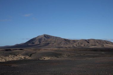 Volkanik kökenli çöl. Bir sürü taş, kaya ve bir tepe var. Mavi yay gökyüzü ve ışık bulutları. Lanzarote, Kanarya Adaları, İspanya.