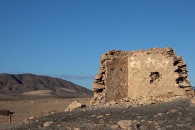 Doğası gereği Playa del Papagayo 'nun yukarısındaki bir tepede bulunan bir borazan yıkıntısı. Parlak mavi gökyüzü. Evin etrafı volkan çölü ile çevrili. Lanzarote, Kanarya Adaları, İspanya.