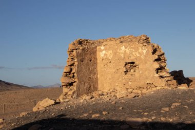 Doğası gereği Playa del Papagayo 'nun yukarısındaki bir tepede bulunan bir borazan yıkıntısı. Parlak mavi gökyüzü. Evin etrafı volkan çölü ile çevrili. Lanzarote, Kanarya Adaları, İspanya.