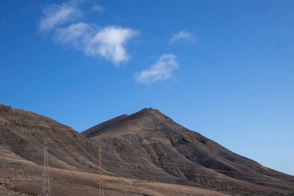 Desert of a volcanic origin with many stones and rocks and a hill. Blue spring sky with light clouds. Lanzarote, Canary Islands, Spain.