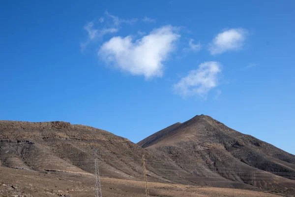 Desert of a volcanic origin with many stones and rocks and a hill. Blue spring sky with light clouds, one of them in a shape of a heart. Lanzarote, Canary Islands, Spain.
