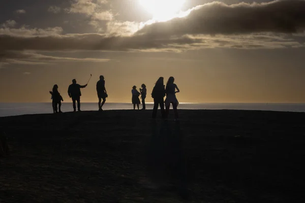 Group of people in the opposite light, enjoying their time of a beginning of the sunset. Hoirzon of the Atlantic ocean and a cloudy sky. Hill at Playa del Papagayo, Lanzarote, Canarian Islands, Spain.