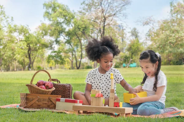 Mutlu etnik kızlar açık hava parkında ahşap blok yap-boz oynuyorlar. İlişki kuran küçük çocuklar, çeşitli etnik kavramlar..