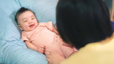 Beş aylık Asyalı bebek annesine bakıyor ve gülümsüyor. Aile kavramı..;