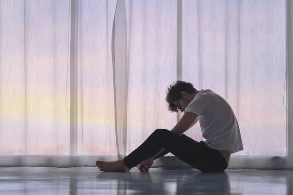 Depresyondaki beyaz adam işini kaybediyor ve aynı zamanda kalbi kırılıyor. Akşamları pencerenin kenarında, düşük aydınlık bir çevrede oturuyor. Travma sonrası stres bozukluğu, zihinsel sağlık ve depresyon kavramı..