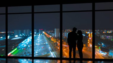 Akşam şehrine karşı panoramik pencerenin yanında duran çift