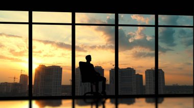 Şehrin arka planında panoramik pencerenin yanında oturan adam.