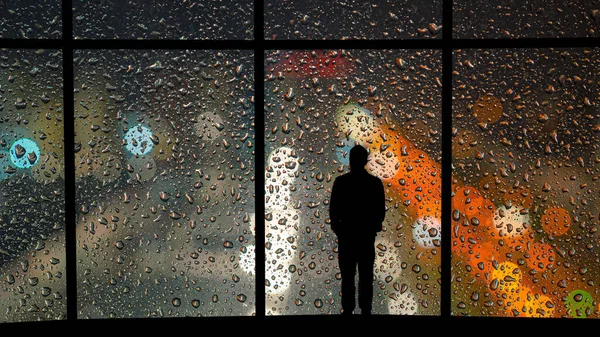 The man standing near the panoramic window with drops of water