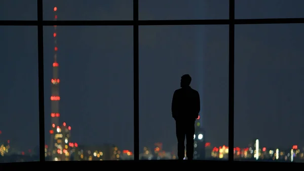 The male standing near the panoramic window against the night city