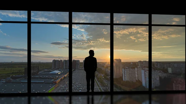 The man standing near the panoramic window on the sunset background