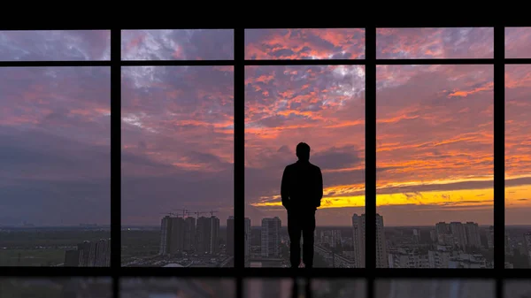 The man standing near the panoramic window on the city sunset background