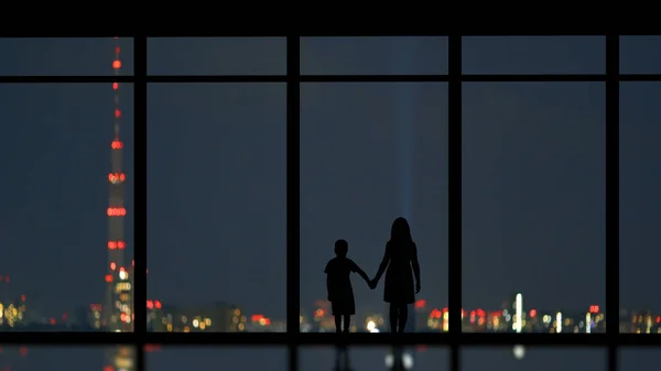 The kids standing near the panoramic window on the city background