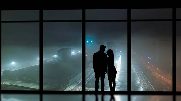 The couple standing near the panoramic window against the night city