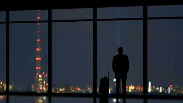 The man with a suitcase standing near a panoramic window on the city background
