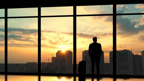 The man with a suitcase standing near a panoramic window against a sunset