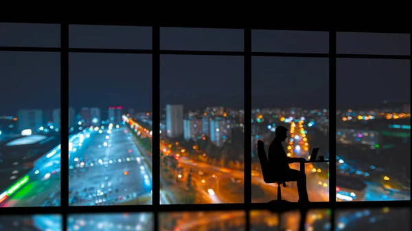 The businessman sitting near the panoramic window on the night city background