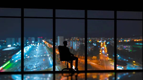 The man sitting near the panoramic window on the night city background