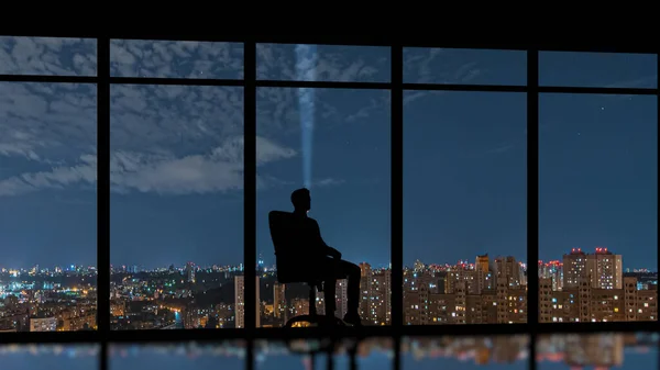 The male sitting near the panoramic window on the night city background