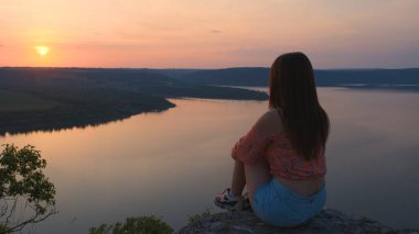 The woman sitting on rocky mountain above the beautiful river