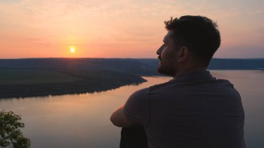 The young man sitting on rocky mountain above the beautiful river