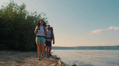 The romantic couple with backpacks walking along the coast