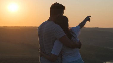 The romantic couple standing on mountain top on sunset background