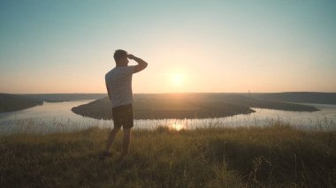The man standing on a mountain top on a beautiful river background