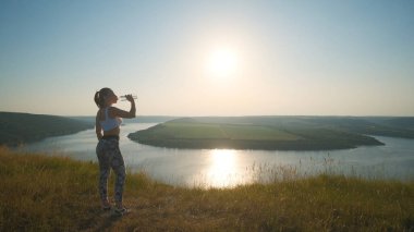 The sportive woman drinking water on a beautiful river background