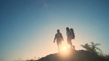The man and woman standing on a mountain top on a blue sky background
