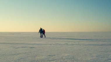 The two people walking through the endless snow field