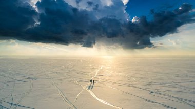 The two people with backpacks walking through the huge snow field
