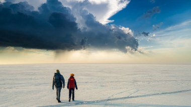 The two people with backpacks walking through the huge snow field