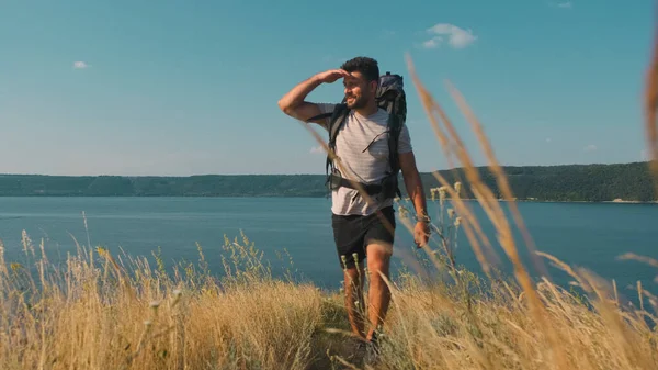 The handsome man walking with backpack along the coast