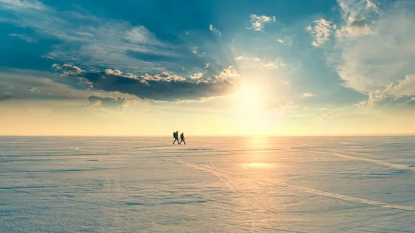 The two travelers going through the snow field on sunshine background