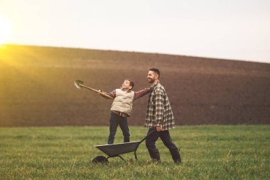 The handsome farmer carrying his son on a wheelbarrow