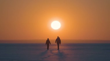 The man and woman going on the snow field on sunset background