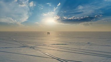 The two people with backpacks going trough the snow field