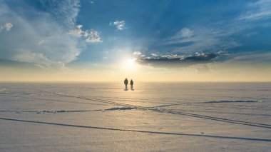 The two travelers with backpacks going trough the snow field