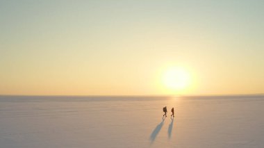 The two people with backpacks going through the snow field against beautiful sky